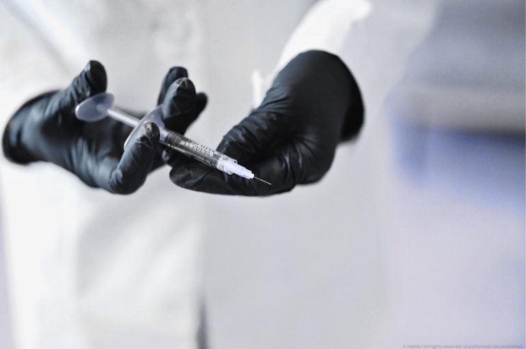Black-gloved hands holding a syringe in a clinical setting