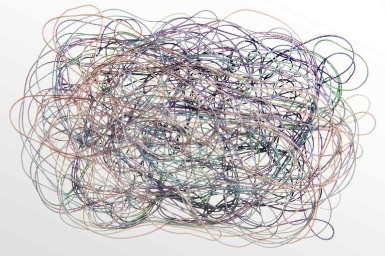 Abstract macro photograph of densely interwoven multicolored threads forming a complex tangled network on a white background, representing the crosslinked polymer matrix of hyaluronic acid filler and the biochemical complexity of hyaluronidase formulation and degradation
