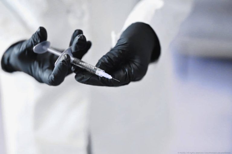 Close-up of gloved hands in black nitrile preparing an injectable syringe in a clinical setting, representing precision and clinical standards at the center of private equity med spa consolidation strategy