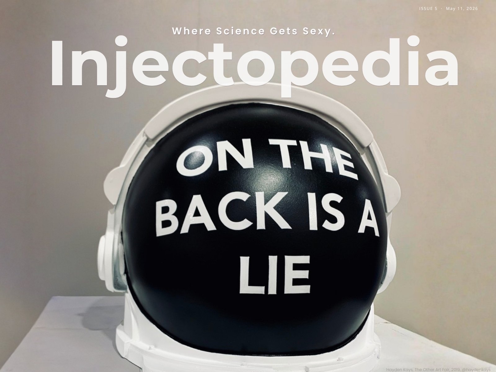 Black astronaut helmet with white text reading "On the back is a lie" by artist Hayden Kays, cover of Injectopedia Issue 5